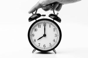 A classic black and white alarm clock being held by a hand, depicting the concept of time.